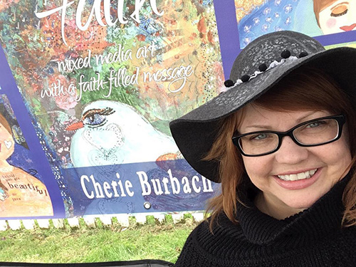 Artist Cherie Burbach poses with some of her work at an art show