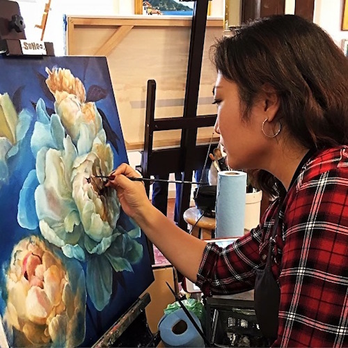 Artist Joyce Lee creating a painting of a peony in her studio.