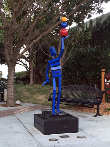 Abstract figurative aluminum sculpture of a blue figure balancing balls by James Moore 