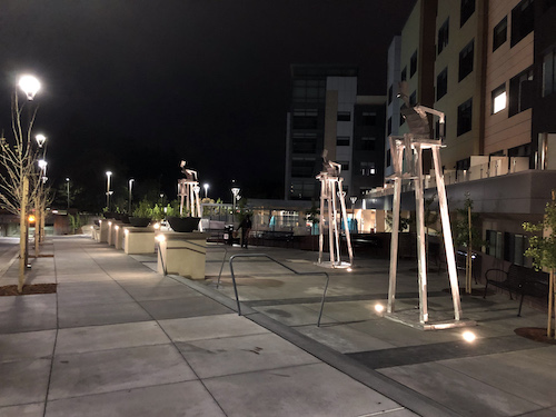 Aluminum sculptures of figures in tall chairs gazing skyward at night by James Moore