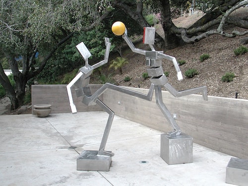 Abstract steel sculpture of two figures playing ball by James Moore
