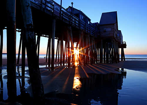 Photograph of the sunrise through the pier at Old Orchard Beach in Maine by Cheryl Harris