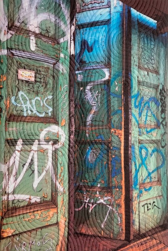 Mixed media quilted fiber art of graffitied doors in Budapest, Hungary by Marilyn Henrion