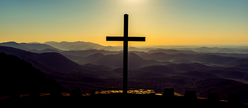 Photograph of a cross silhouetted against the mountains by Luis Almeida