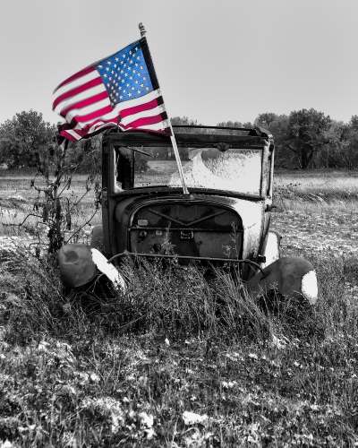 Black & white photograph with color of a dilapidated Jeep with an American Flag by Dave Maes