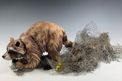 Stoneware and found object sculpture of a raccoon caught in a net by Deana Bada Maloney