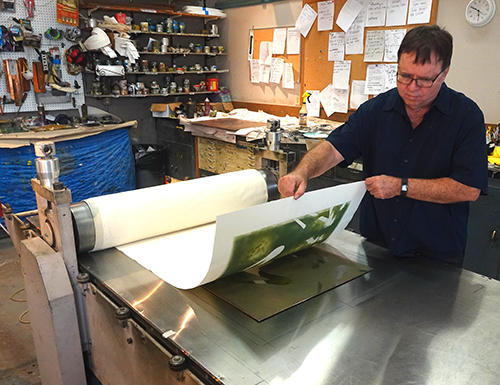 Artist John Costin in his studio pulling an etching