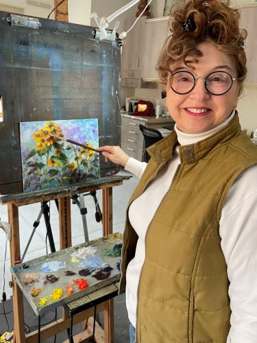 Artist Vic Mastis in her studio with her painting “Sunflower Gathering” 