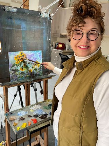 Artist Vic Mastis in her studio with her painting “Sunflower Gathering”